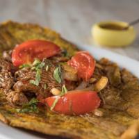 Patacon Salteado · Fried Green Plantain with sautéed chicken or beef, onions, and tomatoes.