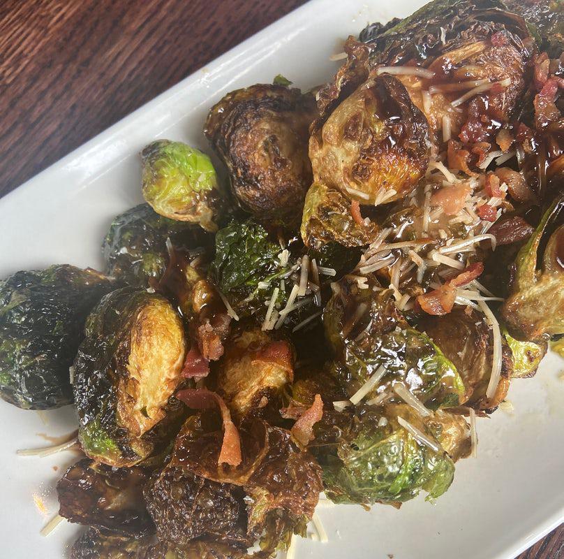 Crispy Brussels Sprouts Appetizer · Flash-fried brussels sprouts tossed with a balsamic dressing and millionaire’s bacon. Garnished with shredded parmesan and a drizzle of balsamic reduction.