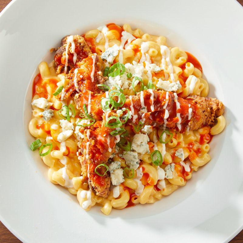 Buffalo Mac & Cheese · A spicy twist on an old favorite. Macaroni and cheese mixed with buffalo sauce, topped with our buttermilk fried buffalo chicken strips. Finished with our creamy ranch dressing, bleu cheese crumbles, and green onions.  For the adventurous!