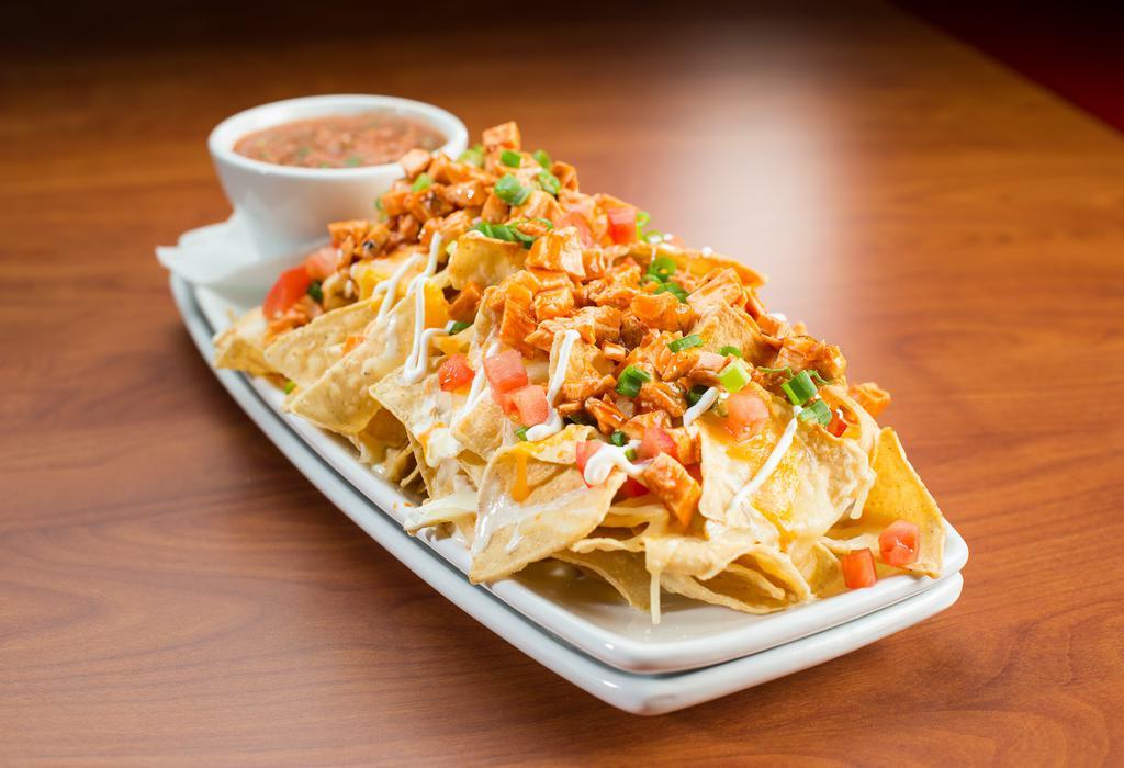 Buffalo Chicken Nachos · Tortilla chips piled high with queso, tomatoes, scallions, sour cream, cheddar jack cheese, and chicken tossed in our hot wing sauce.