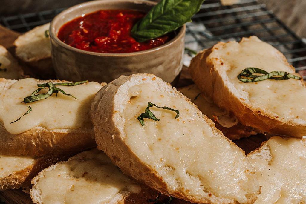 CHEESY GARLIC BREAD · Toasted French baguette, roasted garlic oil, mozzarella, fresh basil, signature red sauce.