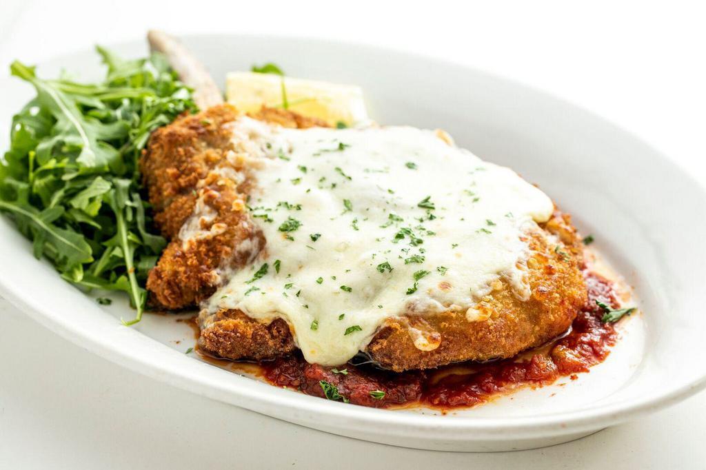 Veal Chop alla Taormina · Breaded veal chop with melted mozzarella cheese on a bed of sautéed tomato sauce and arugula.