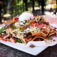 Garlic Shredded Beef Nachos · Crispy corn tortilla chips topped with melted chihuahua cheese, chile con queso, roasted gar...