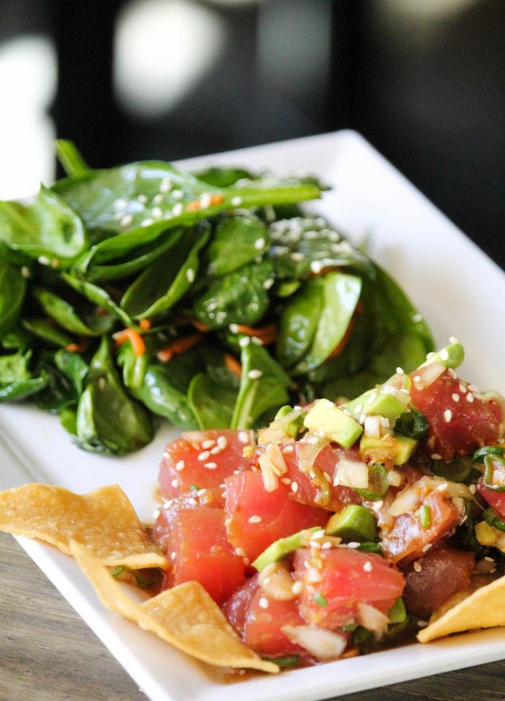 Ahi Poke · Fresh, Grade A Raw Ahi Tuna marinated in sesame soy sauce topped with white onion, green onion, crispy garlic, tortilla chips, sesame seeds, and avocado, served with a spring citrus salad.