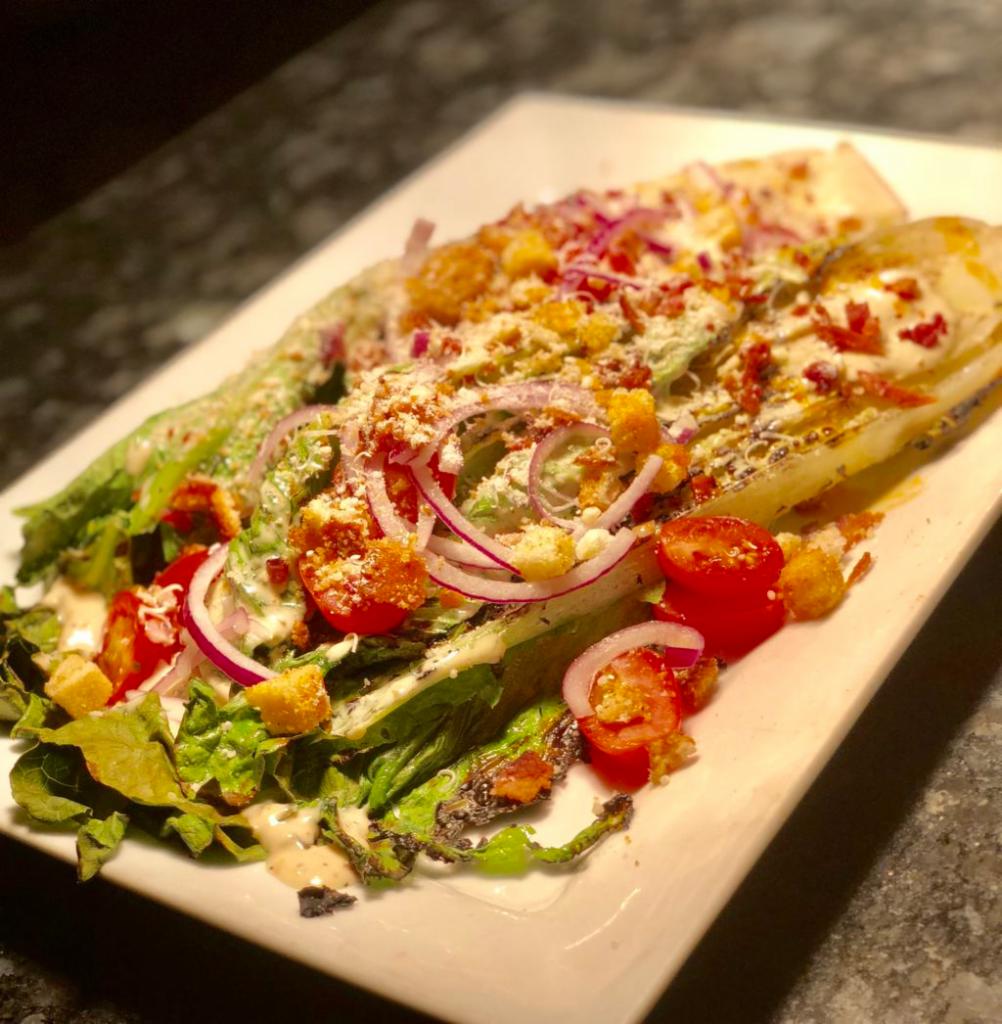 Grilled Romaine Salad · Charred hearts of romaine, bacon, red onions, tomato, Parmesan, crouton, anchovy aioli.