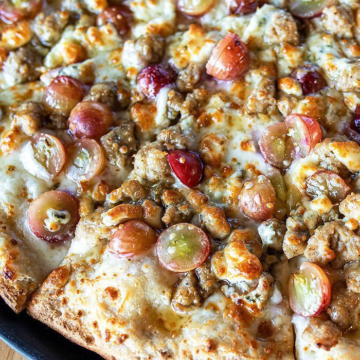 She's No Sour Grape Pizza · Rosemary infused olive oil, mozzarella and Muenster cheese, Italian sausage, sliced red grapes, Gorgonzola, honey drizzle.