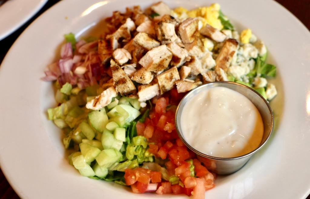 Classic Cobb Salad · Romaine lettuce with grilled chicken, crisp smoked bacon, hard-boiled egg, tomatoes, cucumbers, red onion, avocado and bleu cheese crumbles. Bleu cheese vinaigrette. Gluten free.