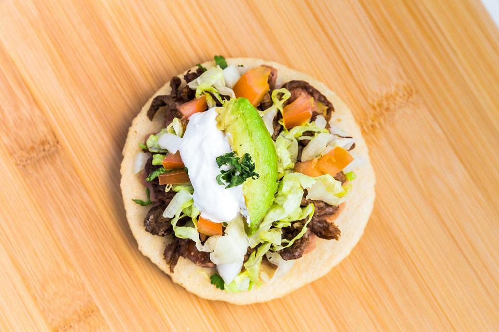 Sope · Beans, onion, cilantro, lettuce, tomato, sour cream, and avocado, showered with hot sauce.