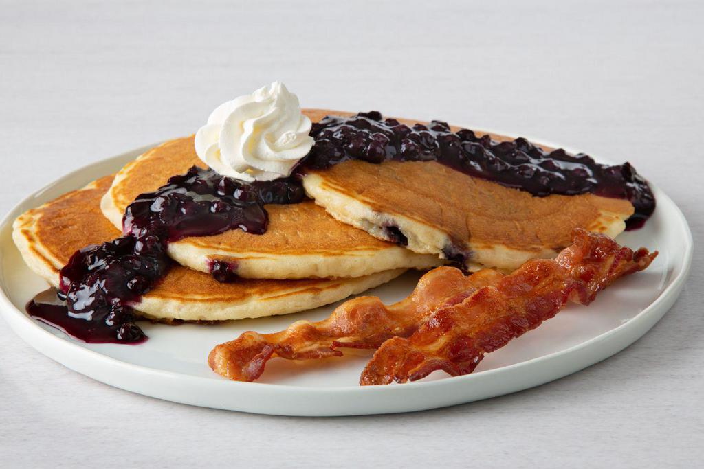 Double Blueberry Pancakes · Three buttermilk pancakes with blueberries, topped with blueberry sauce and whipped cream.  Served with two cherrywood-smoked bacon strips or two sausage links.