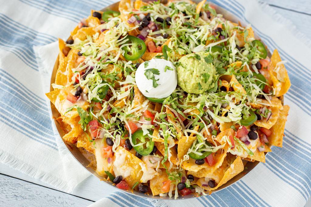 Knock-Out Nachos · Crisp tortilla chips with white cheddar queso & melted cheese blend. Topped with pico de gallo, fresh jalapeños, tomatoes, black beans, shredded lettuce, sour cream, guacamole & cilantro.