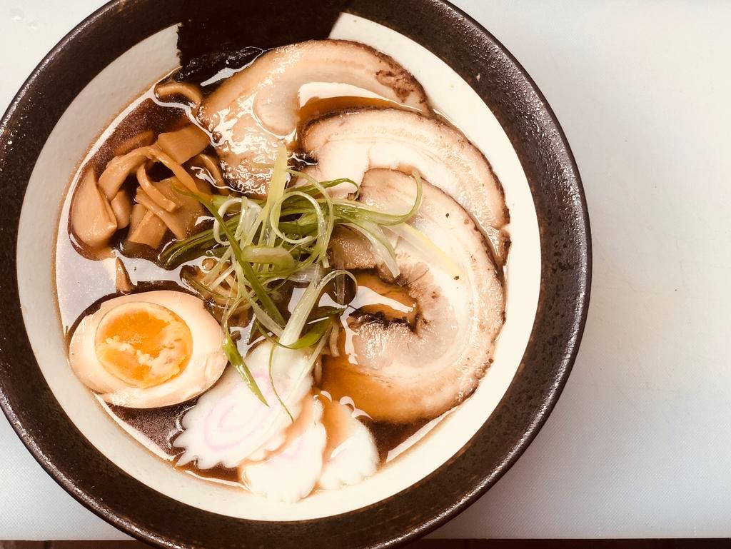 Shoyu Ramen · Soy pork bone broth, wavy egg noodle, topped with chashu pork, shichimi powder, chili & sesame oil, fishcake bamboo shoot, scallion and seasoned boiled egg.