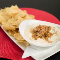 Shredded Pork Queso Dip · Warm white queso dip topped with seasoned shredded pork and served with tortilla chips.