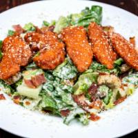Buffalo Chicken Salad · Boneless breaded chicken tenders tossed in Buffalo sauce over a crispy Caesar salad with bac...