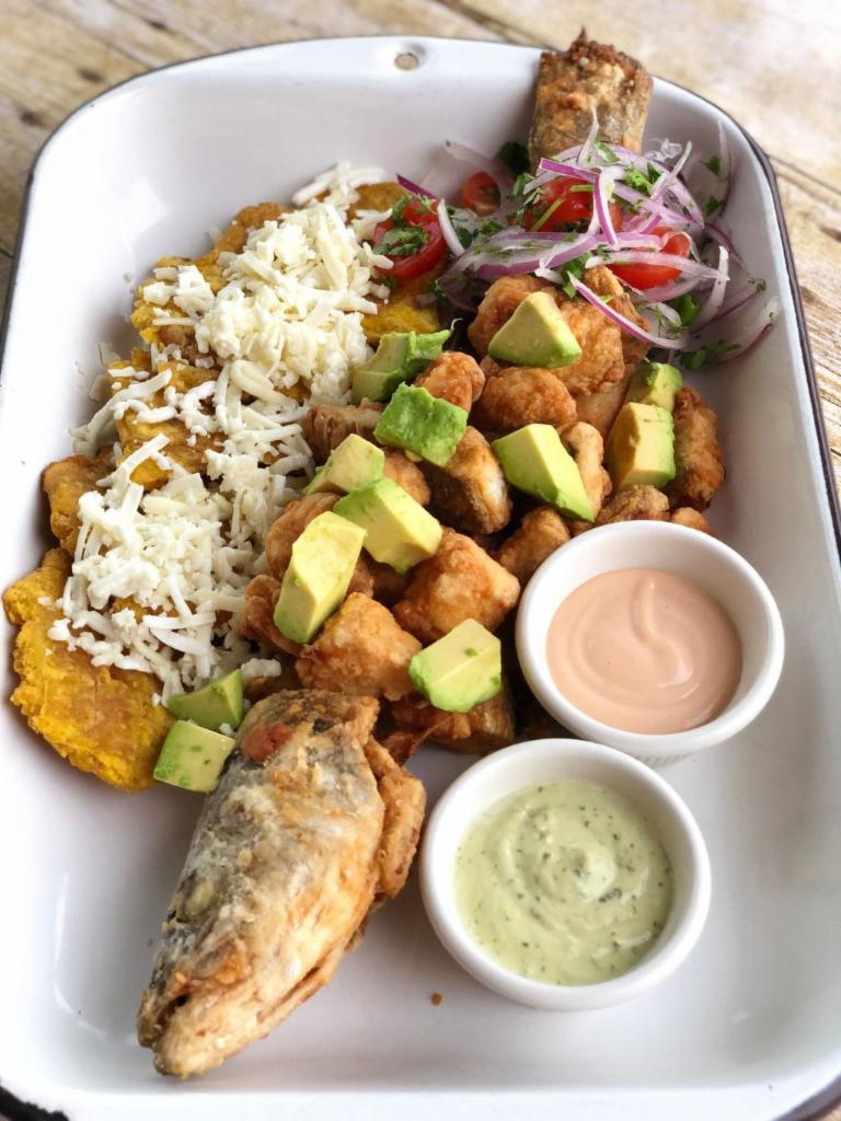 Pescado Frito · Whole deep-fried white fish with fried green plantains, covered with white cheese, avocado, homemade green sauce, pink sauce and sarsa criolla.