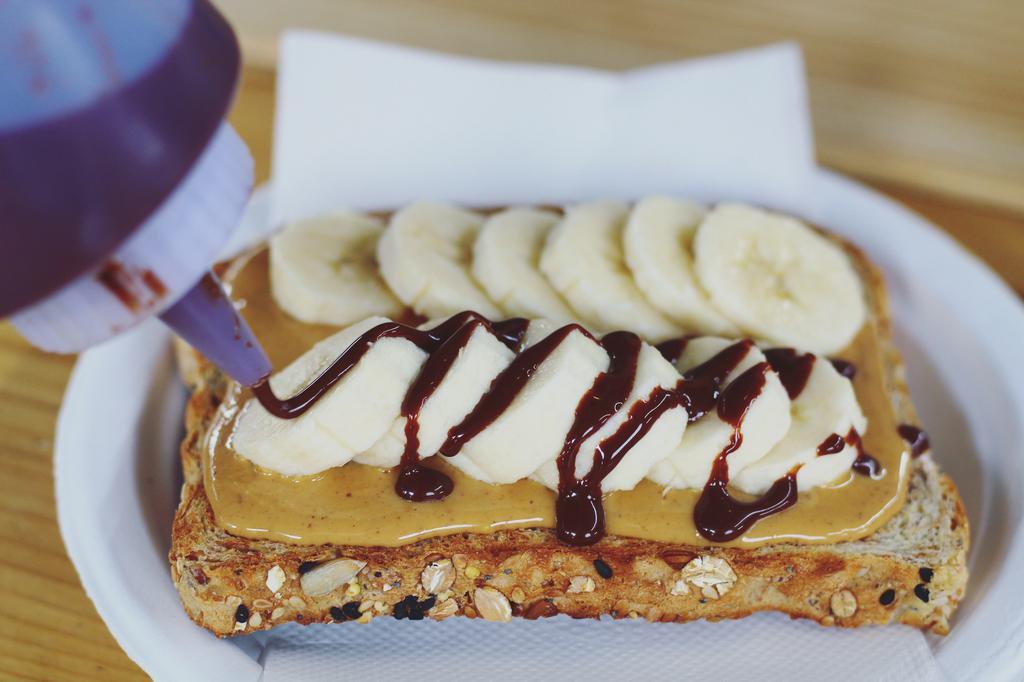 Chocolate Banana Nut Toast · Sprouted organic whole grain bread with almond butter OR peanut butter spread, topped with banana slices, cinnamon, and our house-made dark chocolate drizzle. ** dark chocolate drizzle contains almond butter **