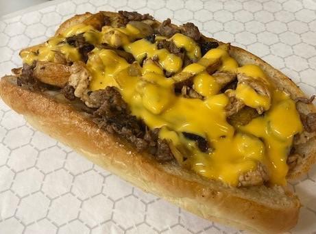Ultimate Cheese Steak · Hand carved Ribeye  steak, grilled sweet onions, White american cheese and cheese sauce on a warm Baguette