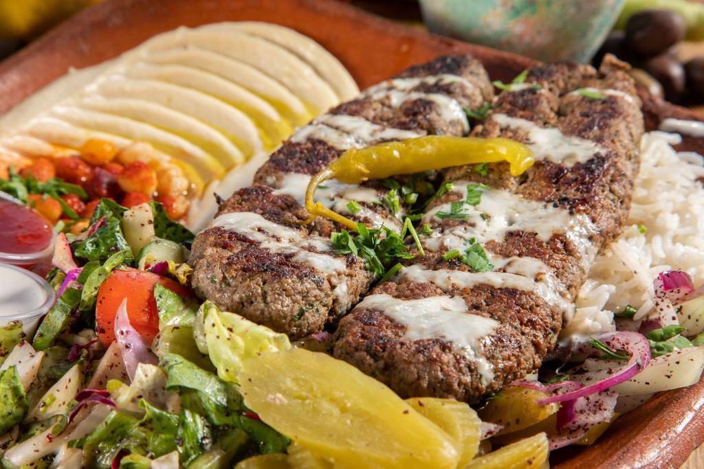 27. Kafta Kabab over Rice Plate · Ground beef with chopped onion and parsley seasoned with a blend of spices, rice, mix salad, tzatziki, hummus and choice of sauce.