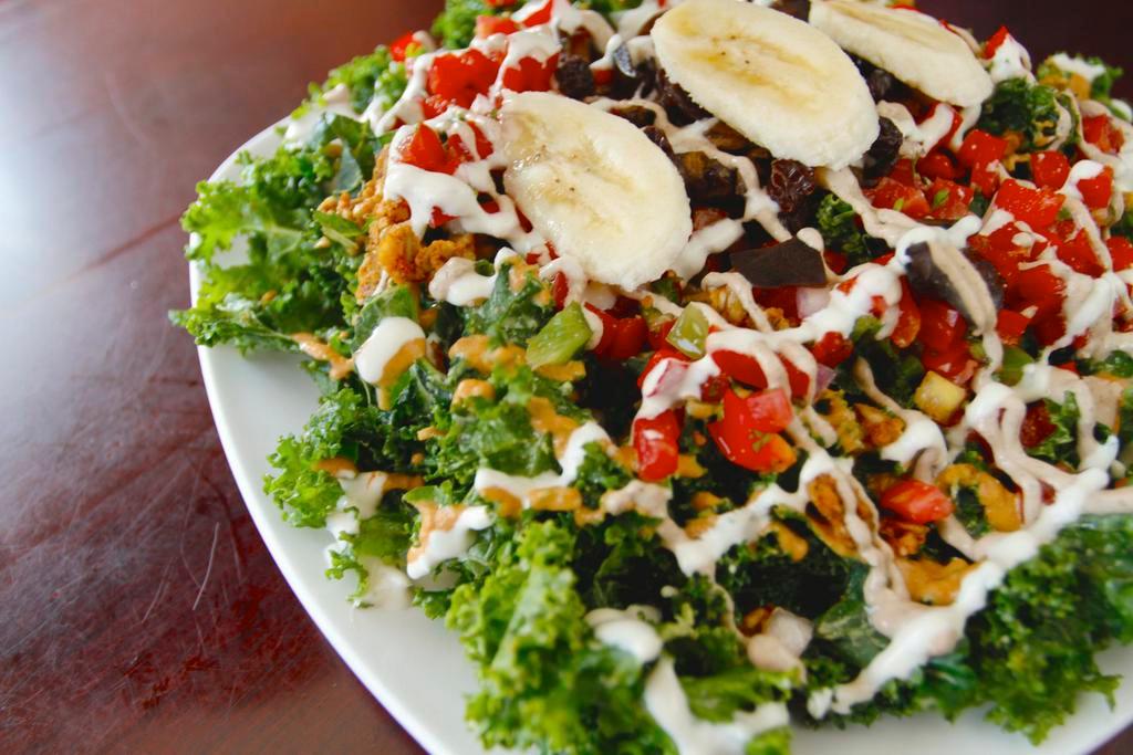 Legendary Kale Colossus Salad · Massaged kale, SunChorizo, marinated mushrooms and bell peppers, pico de gallo, 3 house dressings (nacho, mayo and special sauce), raisins and a crown of banana slices. Raw and gluten free.