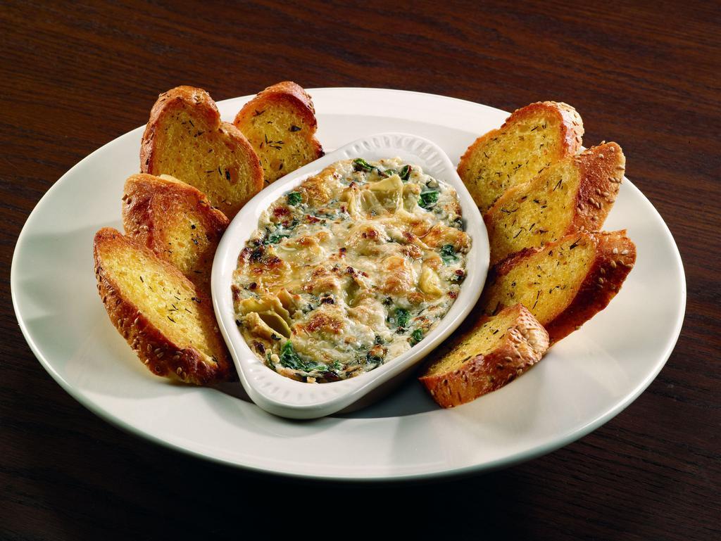 Spinach Artichoke Dip · Fresh sauteed spinach blended with artichokes, mozzarella and Parmesan in a creamy sauce topped with shaved Parmesan and baked. Served with garlic toast points. Lacto-ovo vegetarian.
