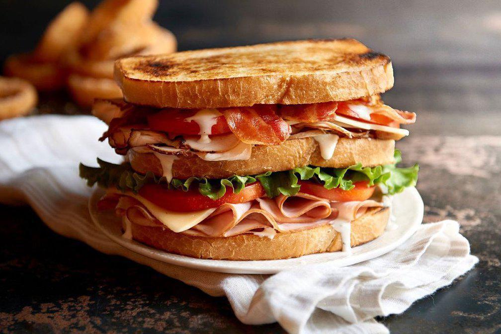 Clubhouse Sandwich · Sliced turkey, ham and smoked bacon topped with provolone and cheddar cheese, fresh greens, tomatoes and garlic aioli on toasted sourdough