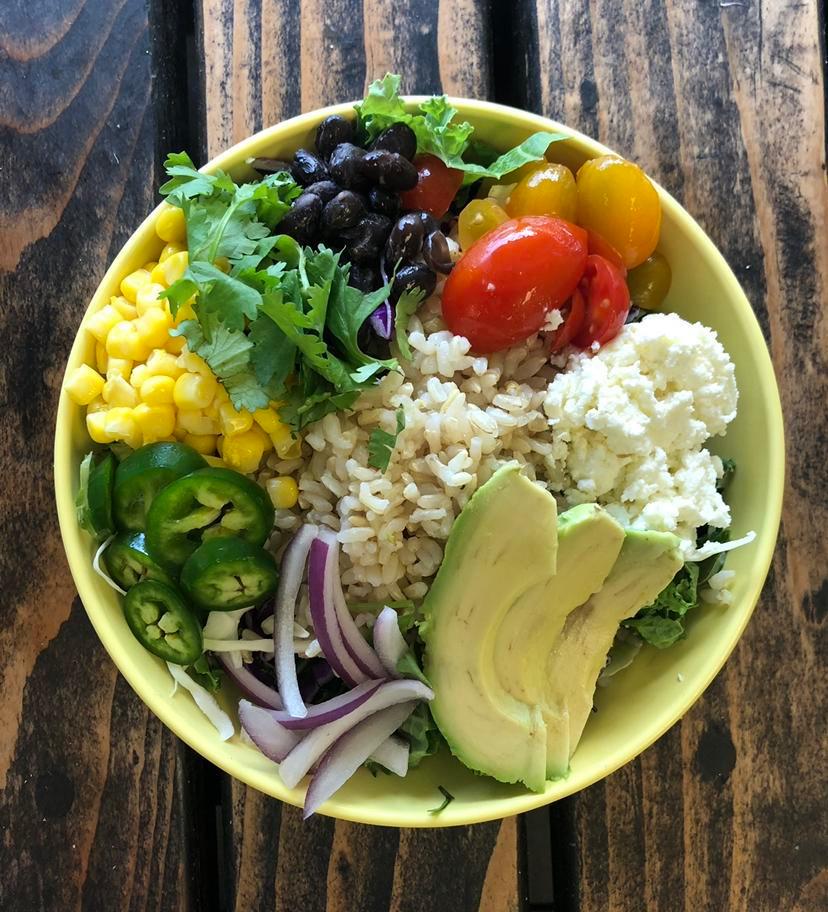 Southwest Buddha Bowl · Grape tomatoes jalapenos red onions corn avocado black beans cilantro feta cheese baby spinach cabbage brown rice and cilantro pepita dressing.