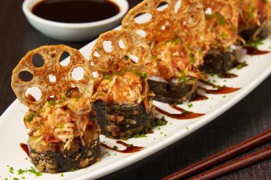 Spicy Lotus Tempura Roll · Krab and cream cheese rolled in rice and seaweed, lightly tempura battered and topped with spicy tuna, krab† mix and sliced lotus root; finished with sweet eel sauce and green tempura bits. 