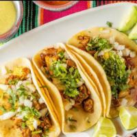 Tacos de Al Pastor · 3 tacos, double tortillas. Marinated pork with pineapple. Sweet and spicy. Topped off with o...