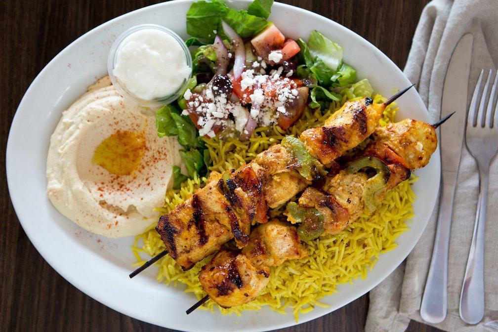 Chicken Kabab · Two skewers of chicken kabab, served with grilled green peppers, and tomato rice, Greek salad, hummus, pita bread and garlic sauce.