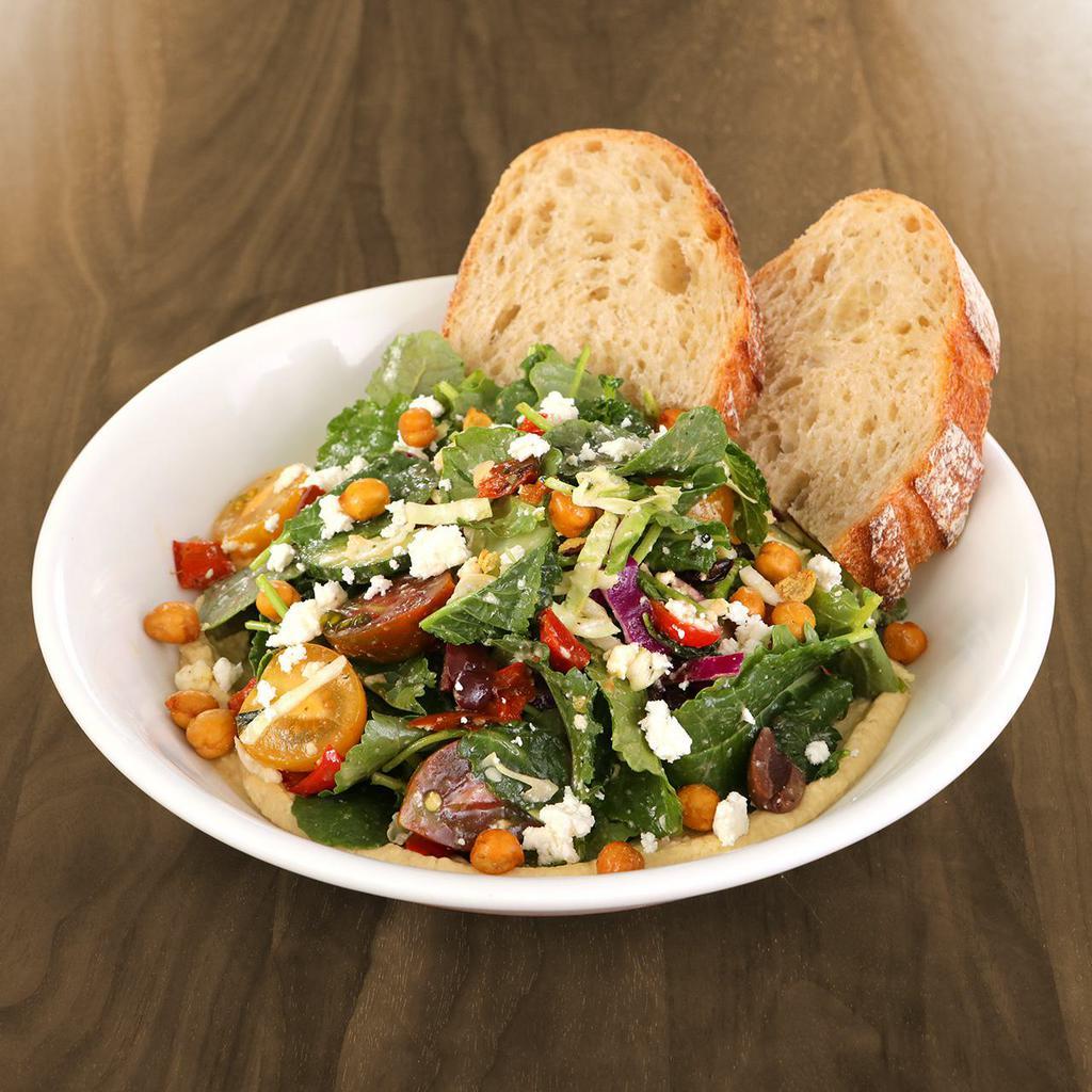 Greek Hummus Salad · organic baby kale, green & red cabbage, heirloom cherry tomatoes, cucumbers, olives, roasted red bell peppers, all-natural feta, roasted chickpeas & all-natural spicy herb vinaigrette served with artisan bread