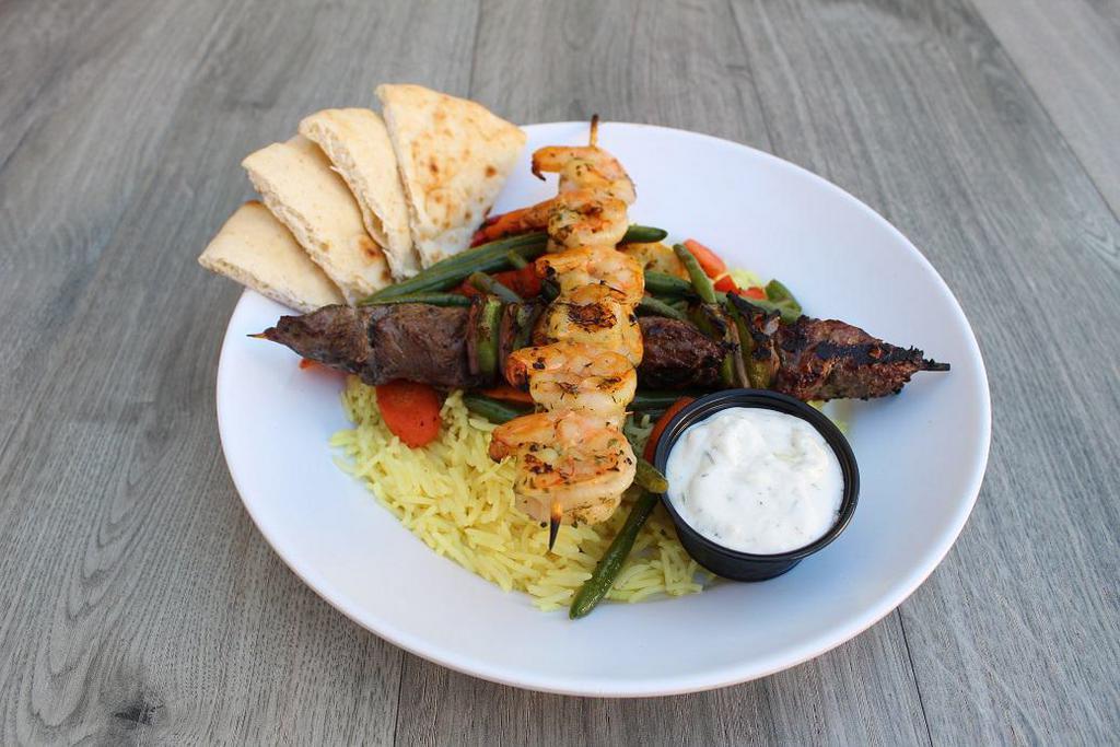 Surf and Turf Plate · Grilled shrimp skewer and steak skewer served on a bed of seasoned basmati rice with roasted vegetables, choice of hummus or tzatziki and warm pita.