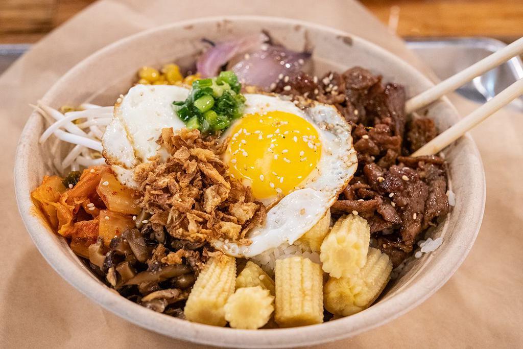Bibimbap · Literally means mixed rice. Slow braised Korean inspired sliced beef with white rice and sauteed sweet onions, homemade kimchi, soy shiitake, sweet roasted corn, and napa cabbage. Roasted sesame seeds, crispy shallots, and spicy gochujang sauce top the bowl off.