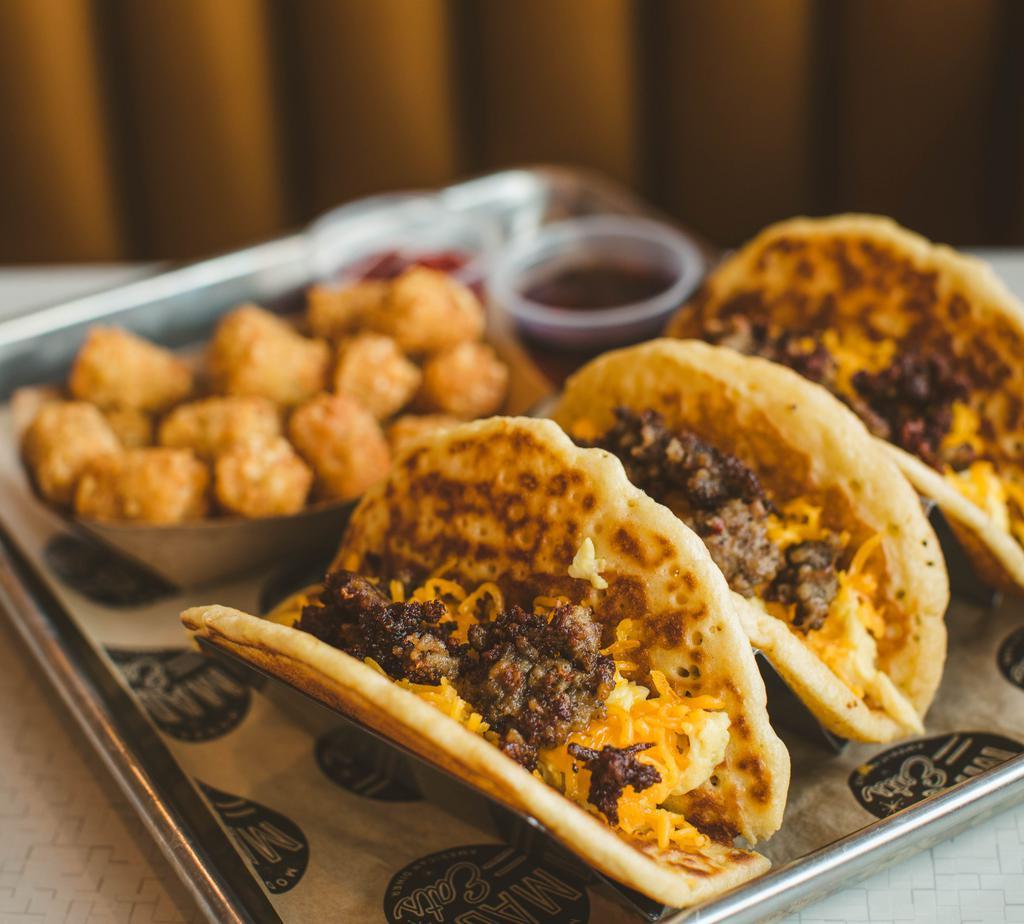 Brunch Pacos · Three buttermilk pancake tacos with scrambled eggs, cheddar cheese and choice of bacon or sausage. Served with maple syrup and hash browns.