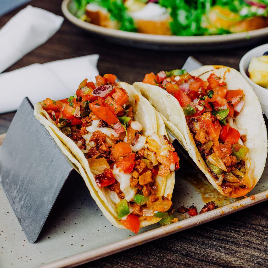 Vegan Tacos  · Choice of vegan chicken strips or vegan chorizo, grilled peppers and onions, cilantro, lime and vegan cheese on white corn tortillas.