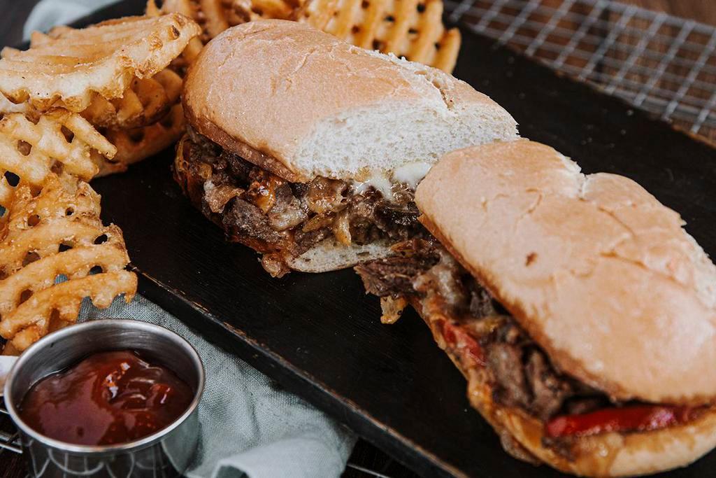 Philly Cheese steak · Shaved sirloin, american + pepper jack cheese, grilled onions and peppers. Served with waffle fries.