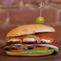 Chivito al Pan · Our signature sandwich: thin slice of New York strip steak topped with ham,  mozzarella, bac...