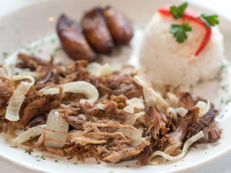 Lechon Asado · Roast pork. Oven roasted shredded pork, marinated and then grilled with sauteed onions. Served with white rice, black beans and sweet plantains.