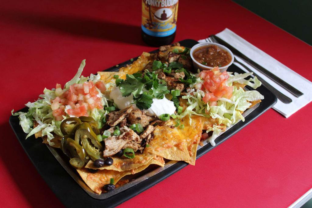 Jerk Chicken Nachos · Corn tortilla chips piled high with jerk chicken, melted cheddar jack cheese, black beans, lettuce, tomatoes, pickled jalapenos, sour cream, green onions, fresh cilantro and served with salsa.