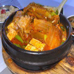 Kimchi Jjigae · Traditional Korean Kimchi stew with assorted vegetables, scallions, soft tofu, and sliced pork belly for a spicy kick of rich flavor.