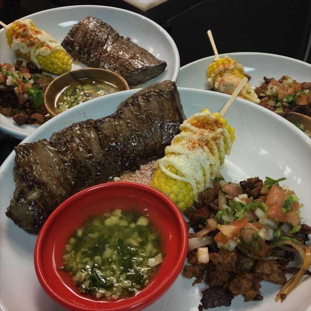 Churrasco Steak · Grilled skirt steak seasoned with Brazilian salt, served with chorizo (Mexican sausage), corn, pico de gallo and a side of chimichurri sauce.