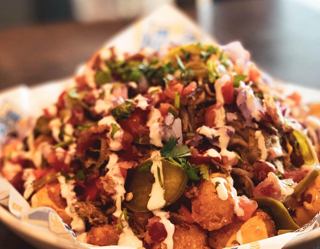Tot Chos · Crispy tots covered in nacho cheese, beer-braised pulled pork, red onion, jalapeno, tomato, sour cream, bacon bits and cilantro.