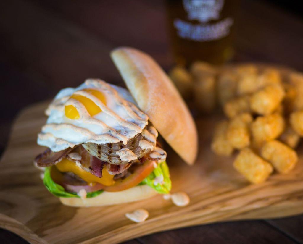 The Hangover Cure Burger · Applewood-smoked bacon, avocado, grilled onion, cheddar cheese, garlic aioli, topped with spicy ranch and a fried egg.