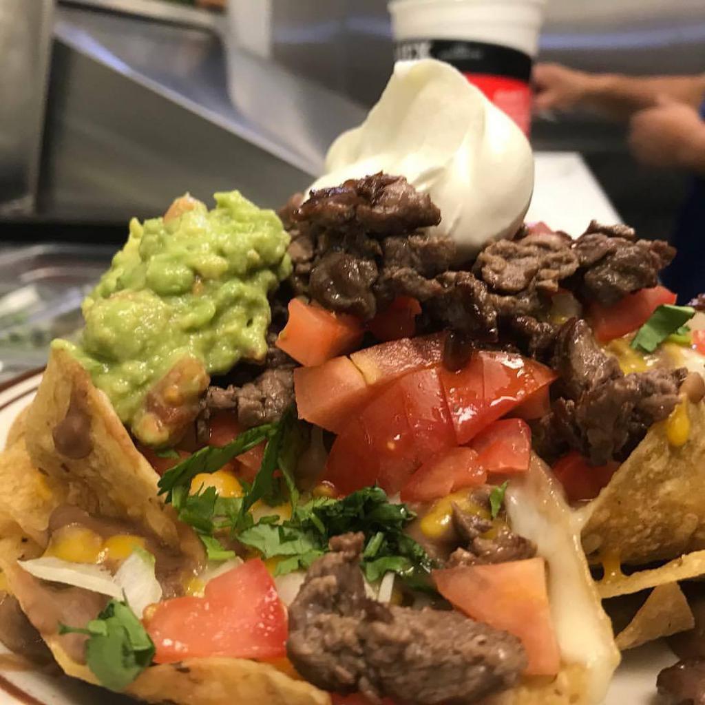 Nachos · Nachos topped with pinto beans, cheese, onions, tomatoes, cilantro, guacamole and sour cream.