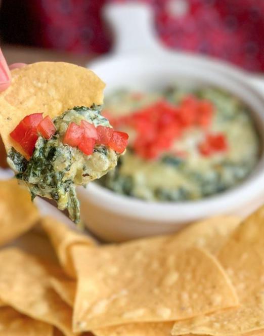 Spinach Dip · Creamy mixture of spinach, artichoke, roasted garlic and Parmesan cheese. Topped with diced tomatoes. Served with fresh tortilla chips.