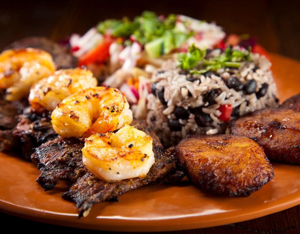 Surf and Turf Dinner  · Succulent garlic shrimp (or salmon) and your choice of sizzling skirt steak or chicken. Served with sweet plantains, cabbage salad, and Gallo pinto.
