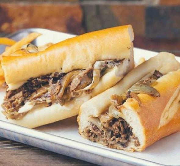 Cheese Steak WIT Moonshine · Classic philly cheese steak made with our signature provolone cheese sauce, American cheese and fried onions. Served with lettuce, tomato and onion on a grilled brioche bun with a side of shoestring fries.