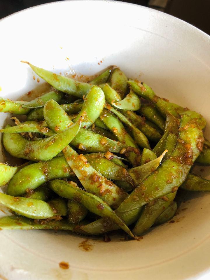 Sweet & Spicy Edamame · Wok seared edamame tossed with sauteed garlic and a sweet & spicy soy glaze, garnished with Peaks seasoning.