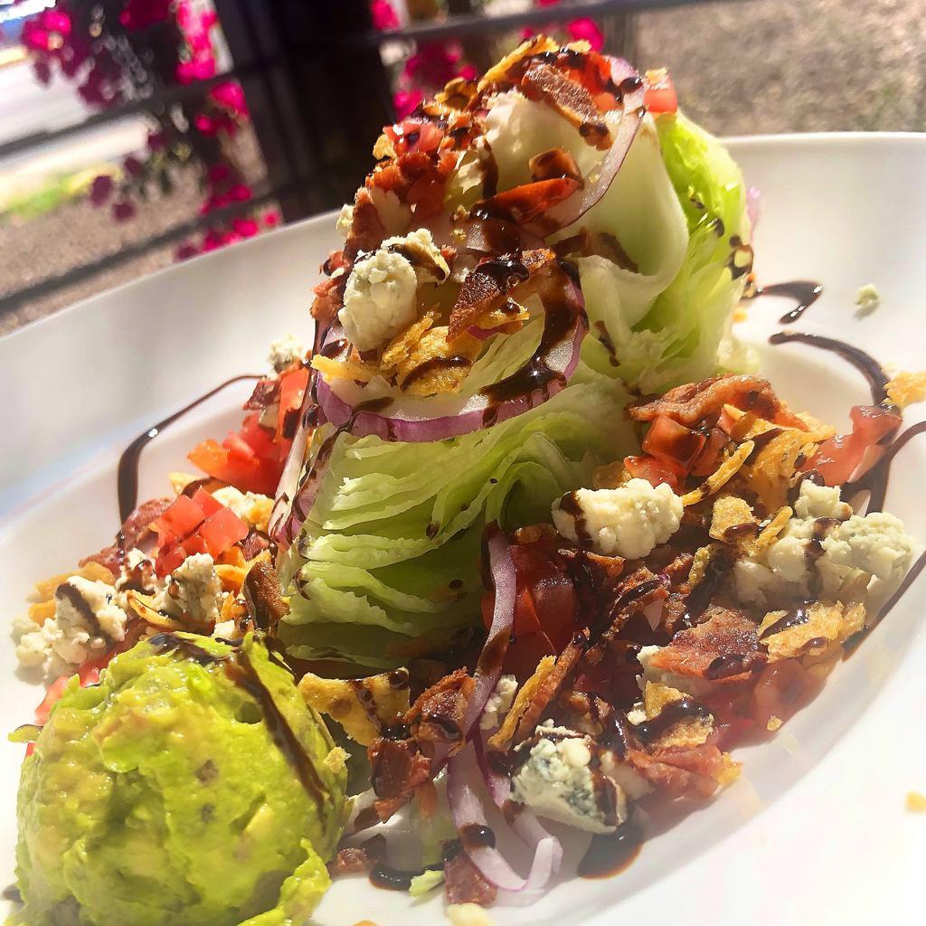 Southwest Wedge · Iceberg wedge topped with smoked bacon, blue cheese crumbles, red onion, diced tomato, guacamole, Fritos & balsamic glaze