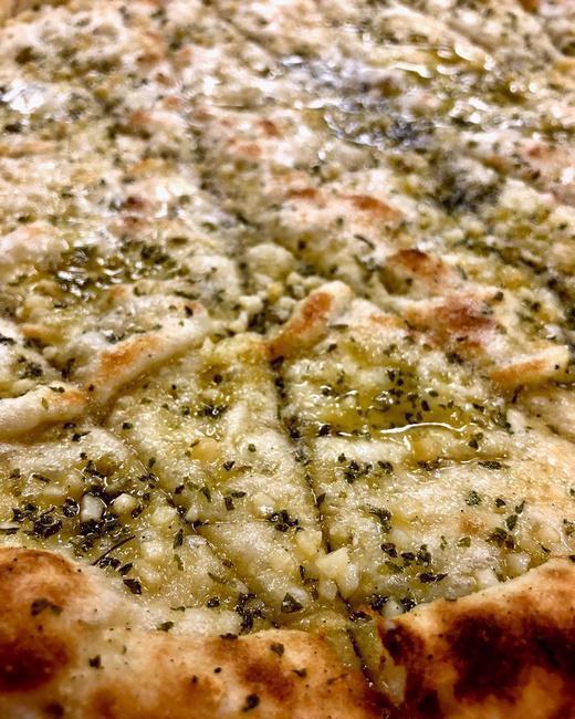 Garlic Bites · Fresh pizza dough topped with garlic & herb butter blend, baked in our wood-fired oven and topped with pecorino romano. Cut into bite sized squares and served with a side of marinara.