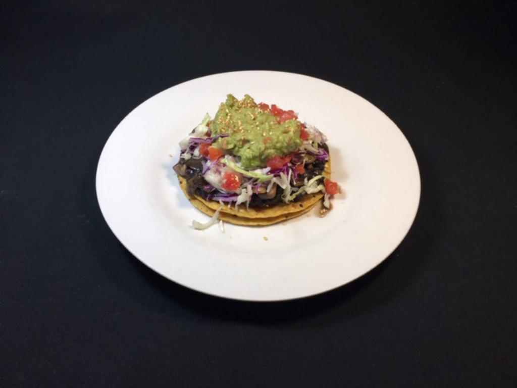 Vegan Tostada · 1 in 2 corn crispy tostadas with sautéed mushrooms, mashed black beans, tomatoes, lettuce and avocado.