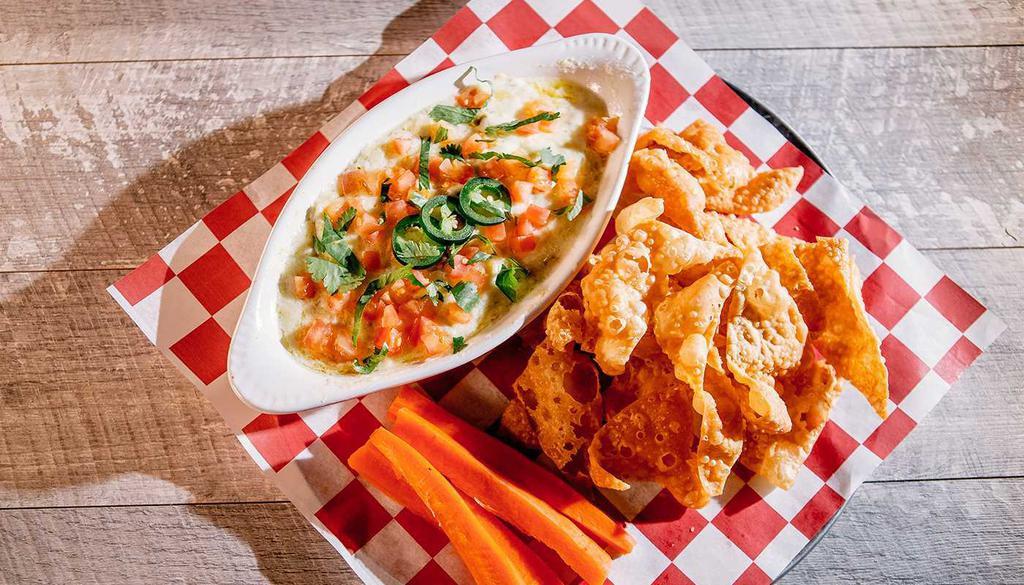 Artichoke Jalapeño Dip · Freshly made creamy, slightly spicy dip with artichokes and jalapeños, topped with tomatoes, jalapeño slices and cilantro – served with wonton chips and carrots.
